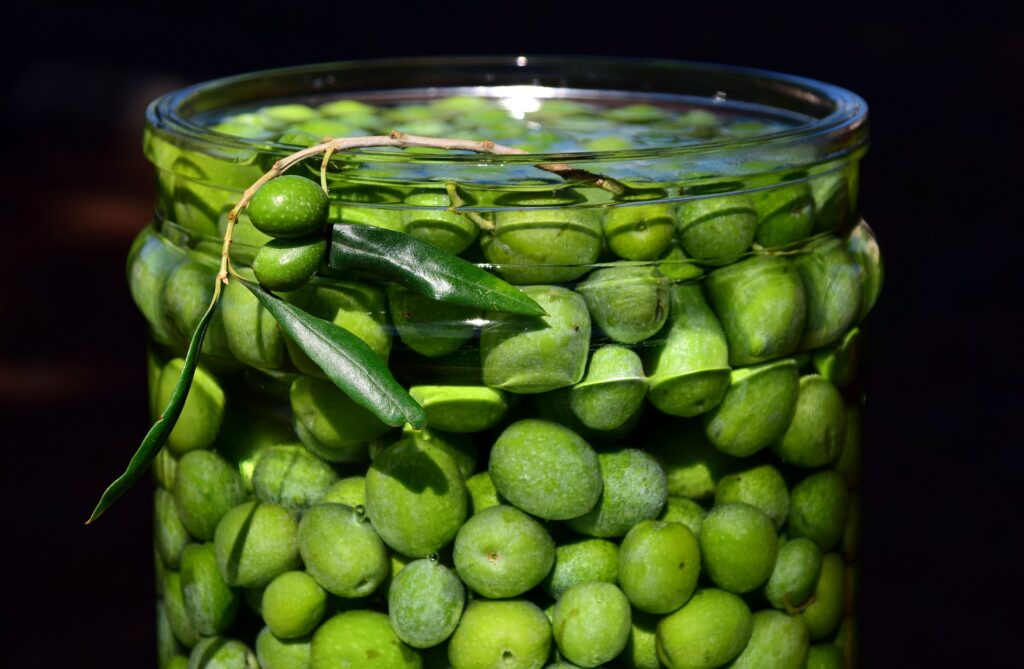 green olives being washed in a jar of water