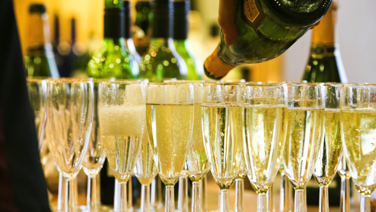 A waiter's hand pouring many glasses of Champagne